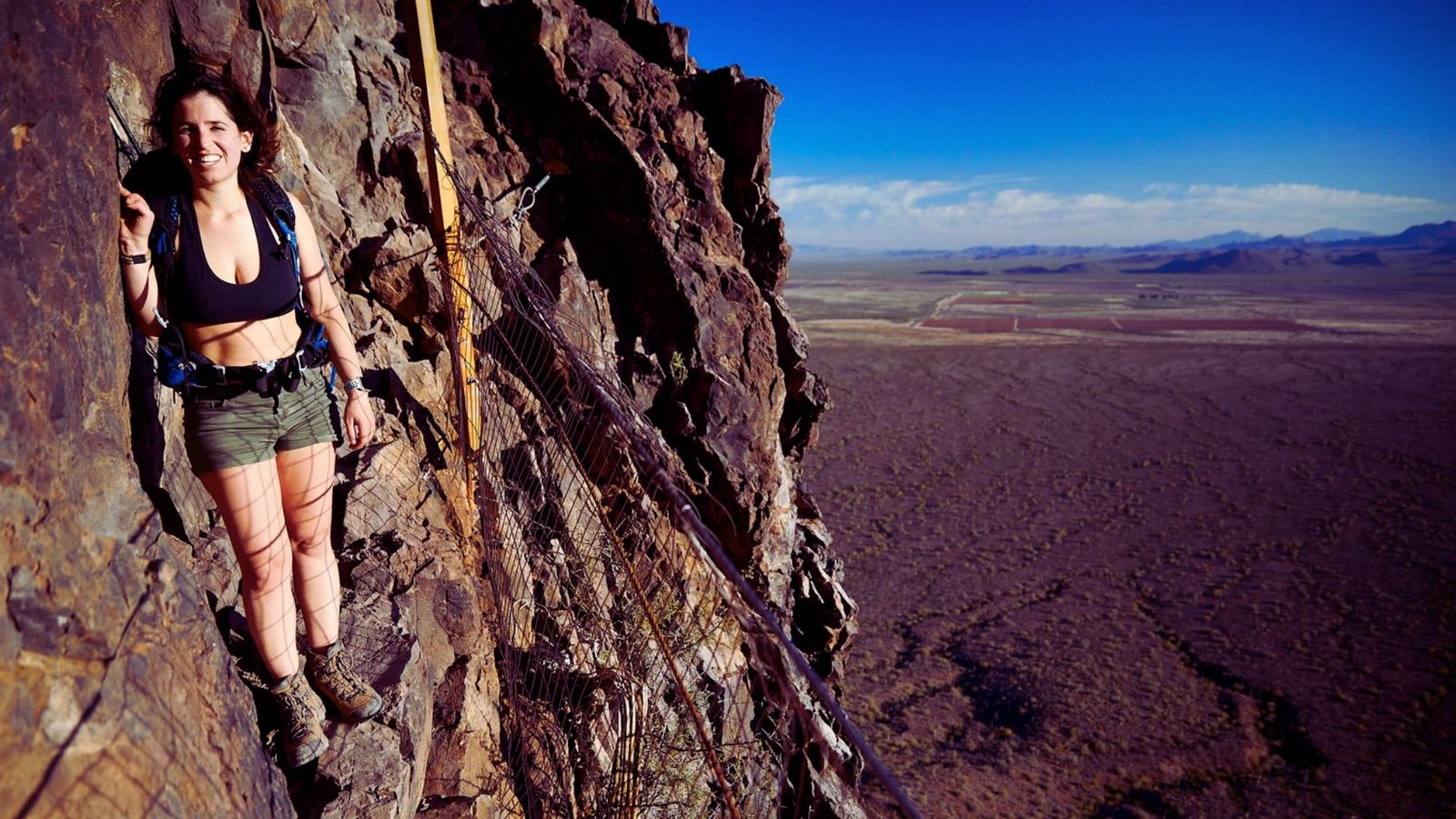 A woman skillfully climbs a steep rock face, showcasing her determination and strength in an outdoor setting.
