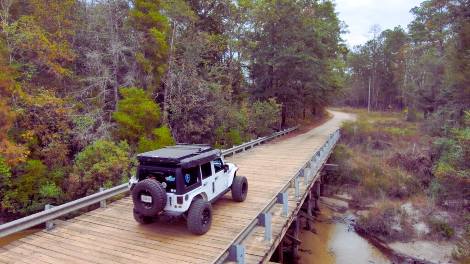 A jeep traverses a wooden bridge surrounded by dense woods, showcasing a scenic outdoor adventure.