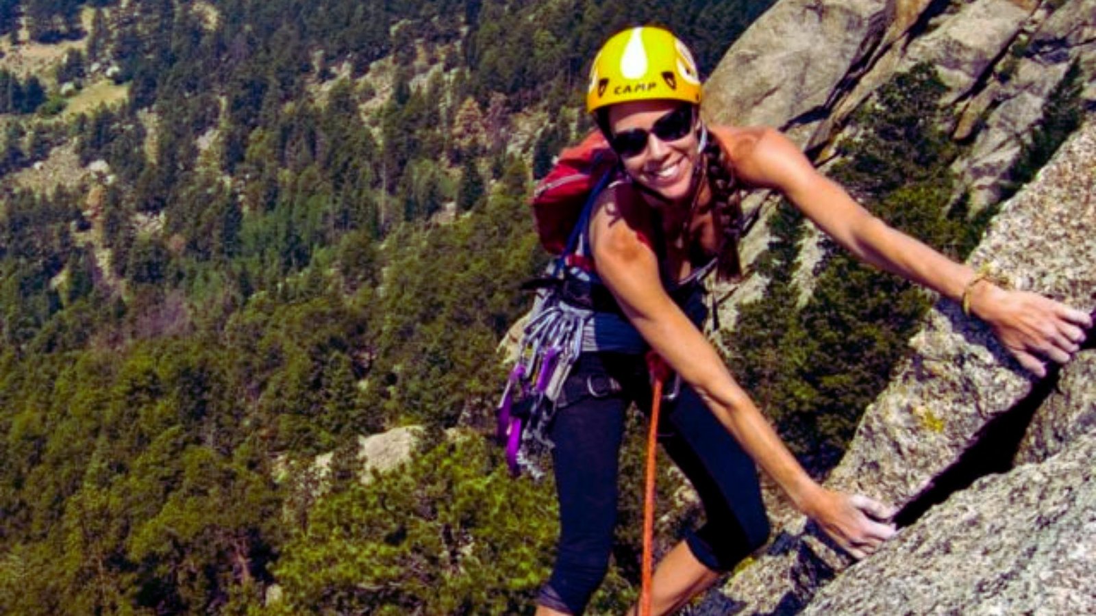 A woman wearing a helmet climbs a rock, demonstrating her skill and determination in outdoor climbing.