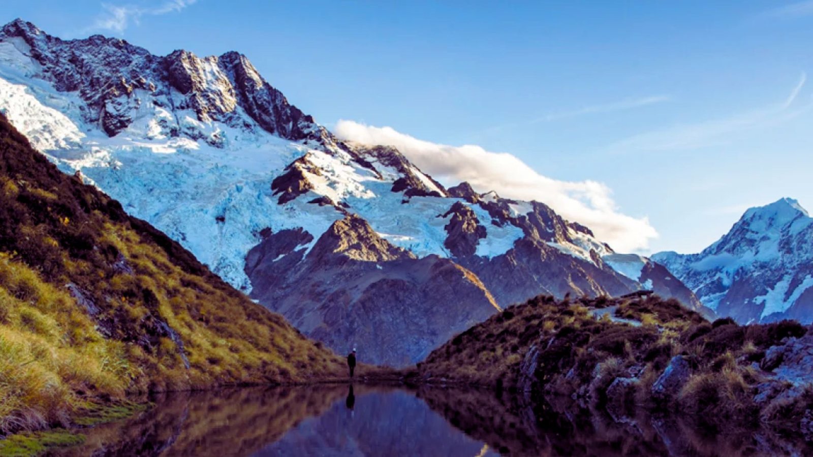 A serene mountain range is mirrored in the calm waters of a river below, creating a picturesque landscape.