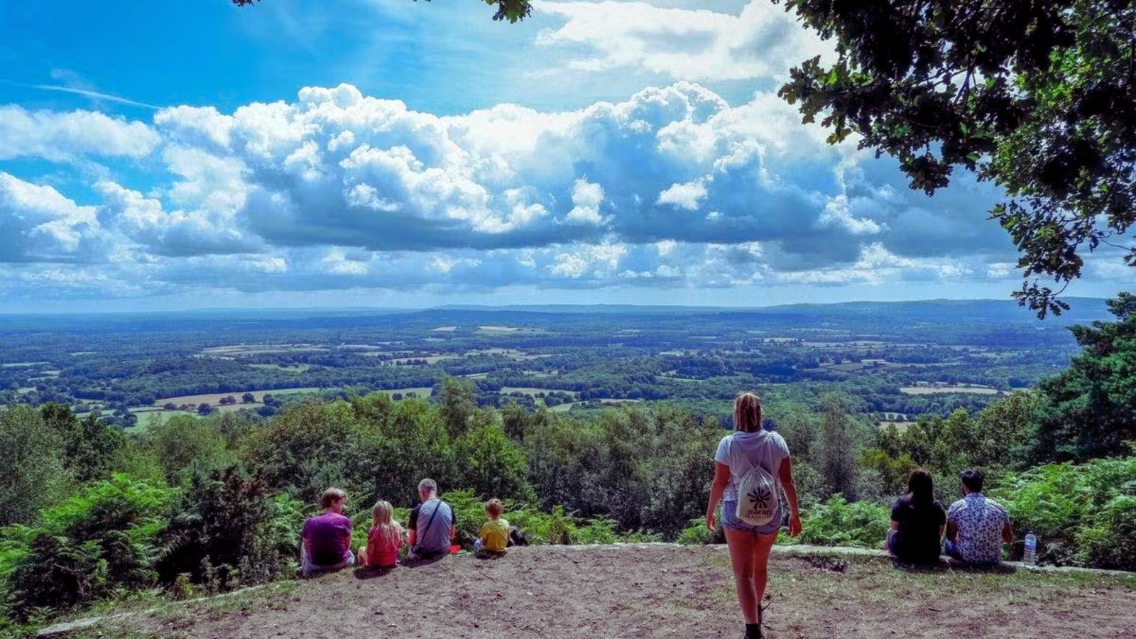 A group of people sitting on a hill, enjoying the view of a lush valley below them.
