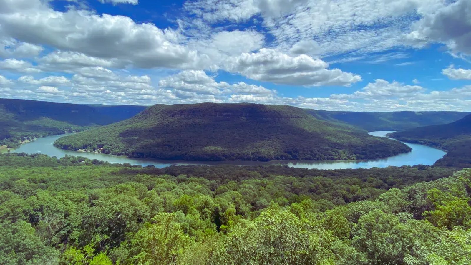 A panoramic view of a river winding through mountains, captured from a high vantage point under a clear blue sky.