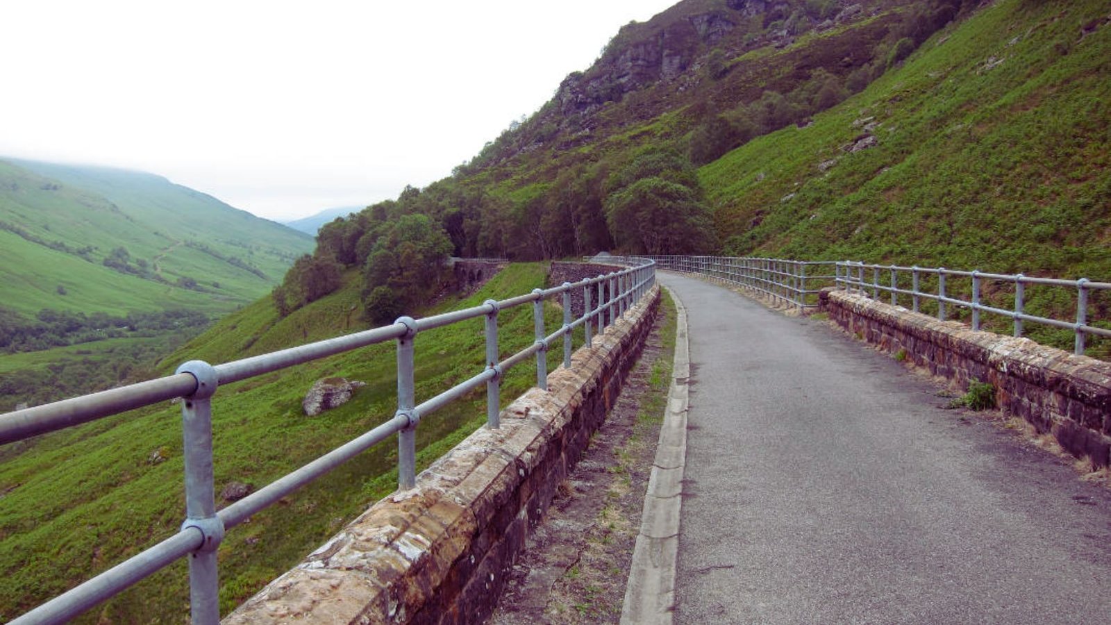 A smooth paved road with a sturdy metal railing alongside for protection.
