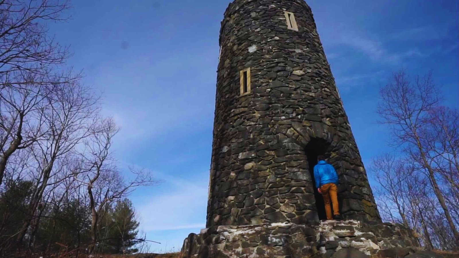 A person poses in front of a stone tower, highlighting its impressive structure and the surrounding landscape.