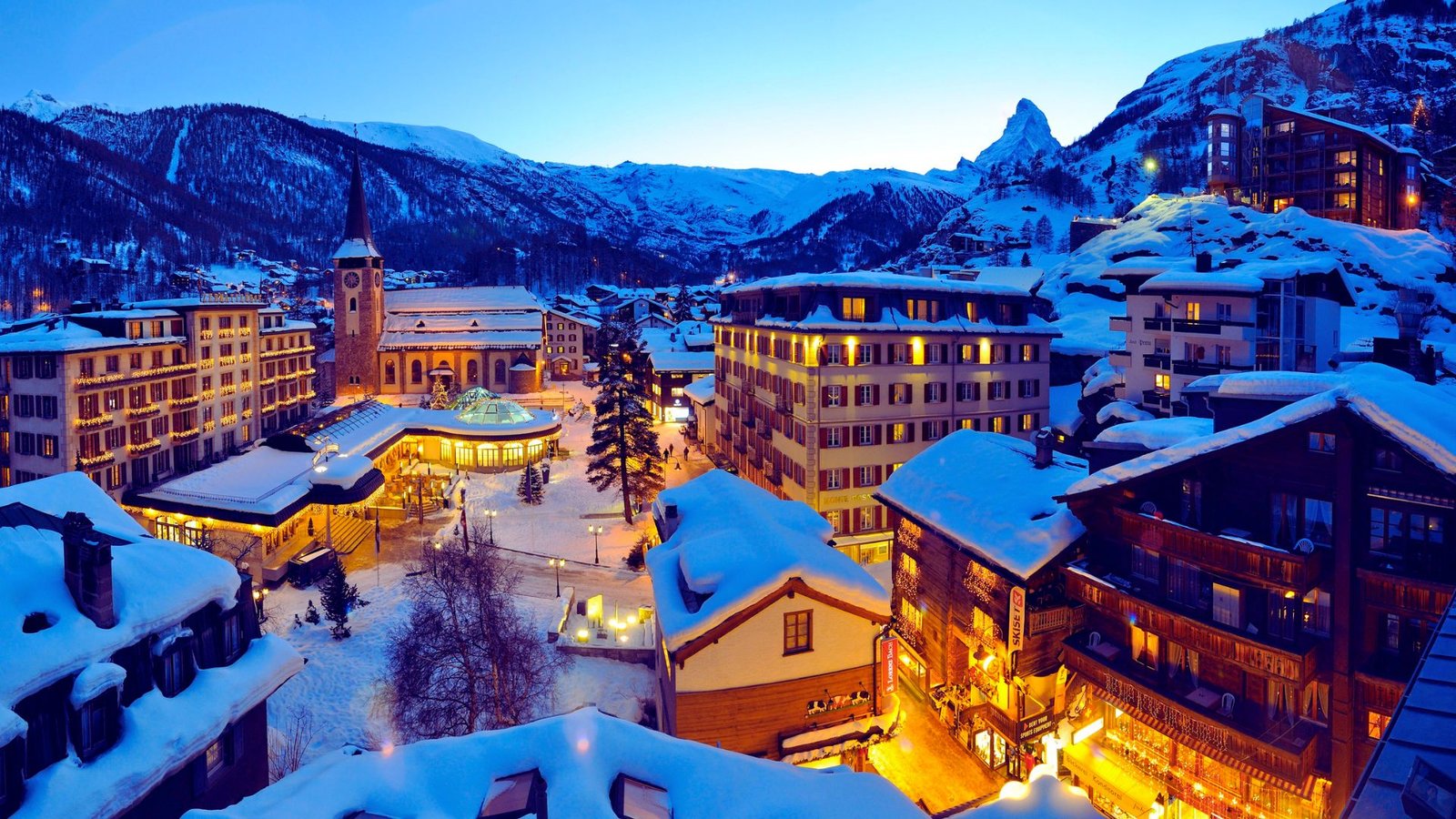 A snowy town scene featuring illuminated buildings and twinkling lights against a winter backdrop.