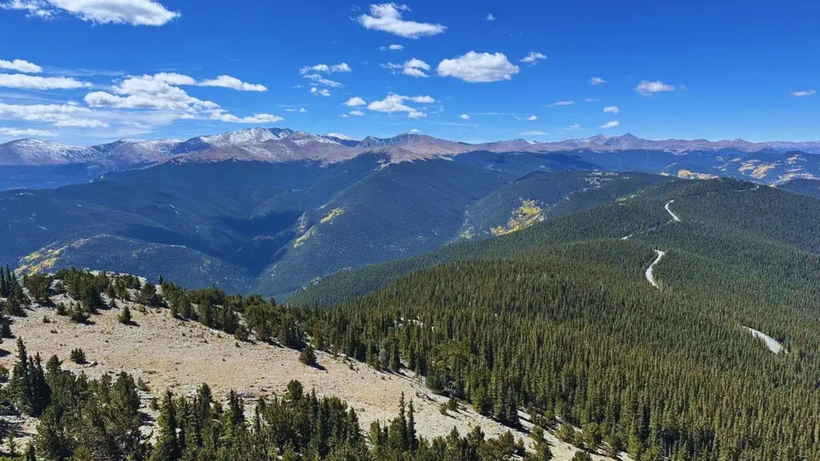Panoramic view from the mountain summit, showcasing vast landscapes and distant peaks under a clear blue sky.