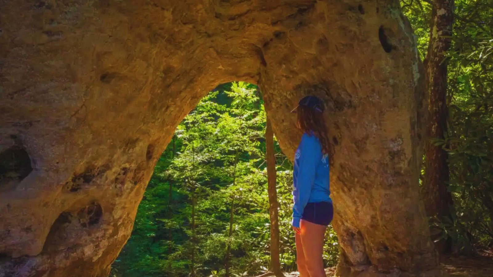 A woman stands confidently in front of a large rock formation, showcasing her connection to nature.