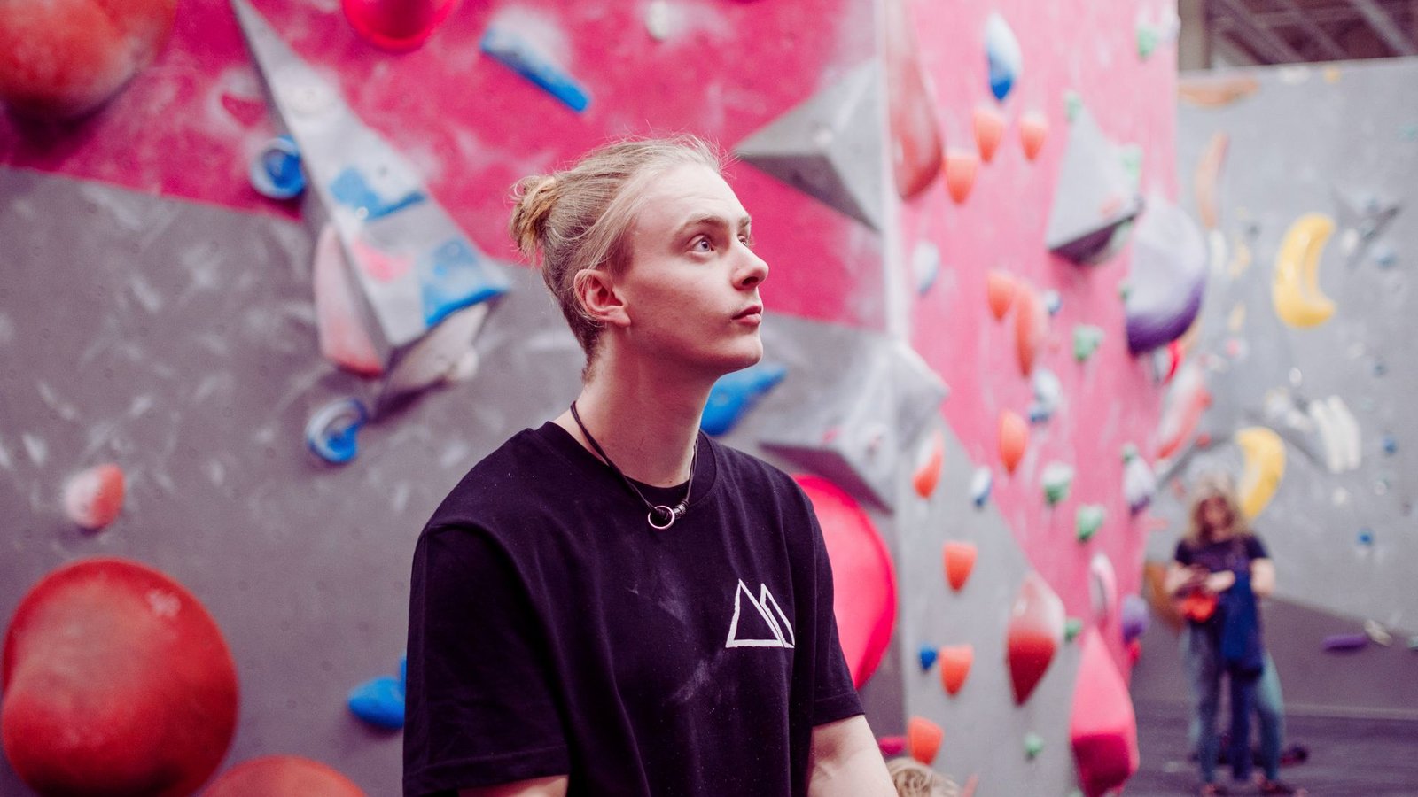 A man stands confidently in front of a colorful climbing wall, ready to begin his ascent.