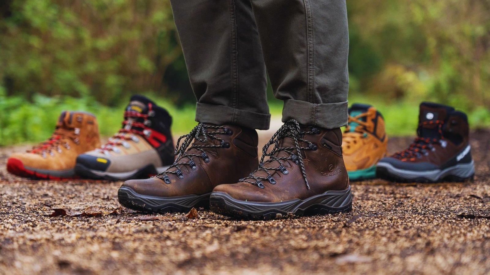 A man stands in front of various hiking boots displayed on a table, showcasing different styles and colors.