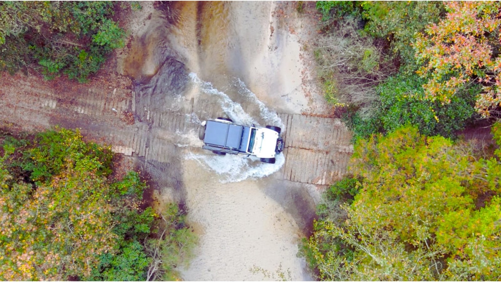 Aerial view of a truck navigating a muddy road, showcasing tire tracks and splashes of mud.