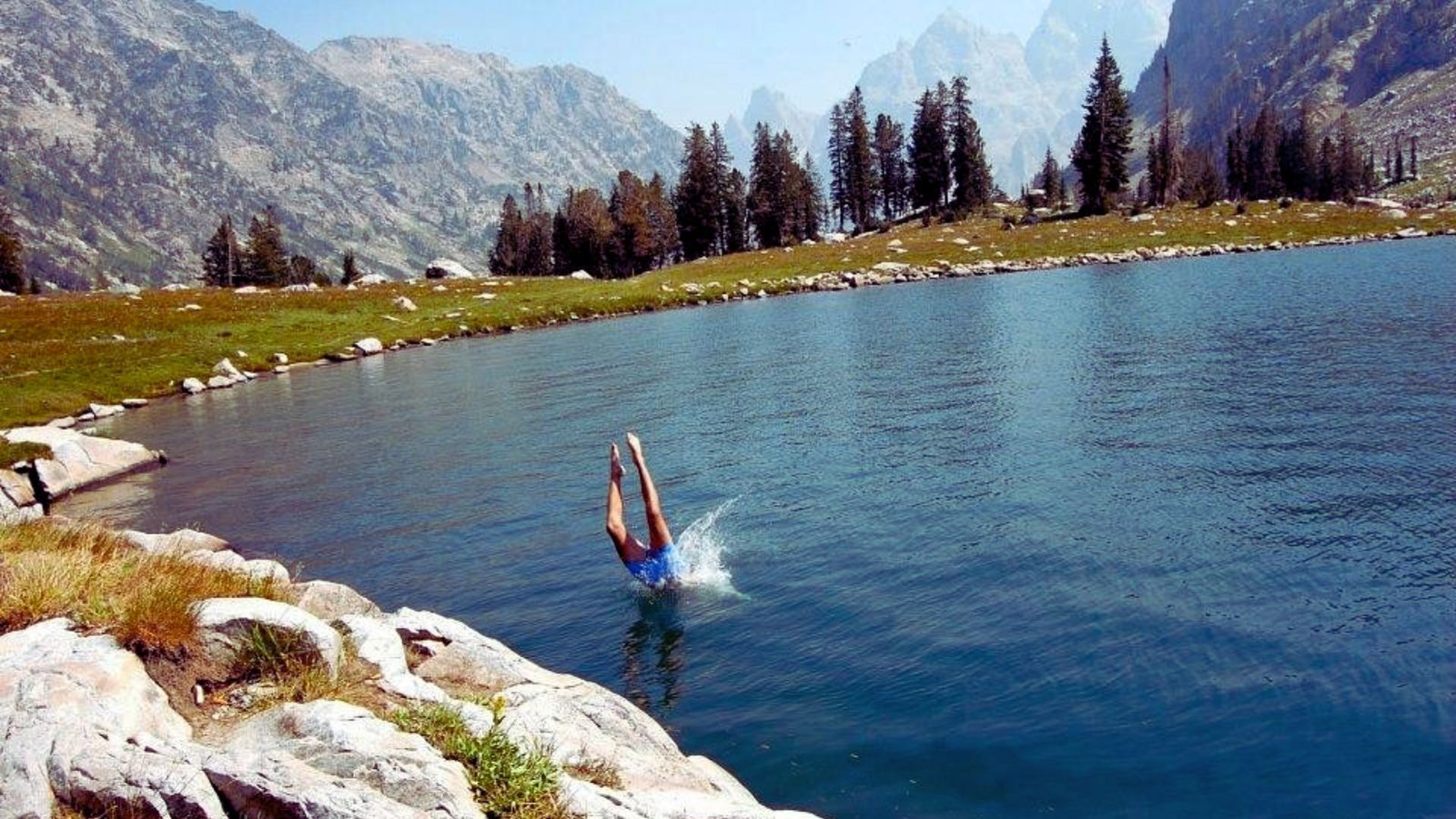 A person diving into a serene lake, surrounded by majestic mountains in the background.