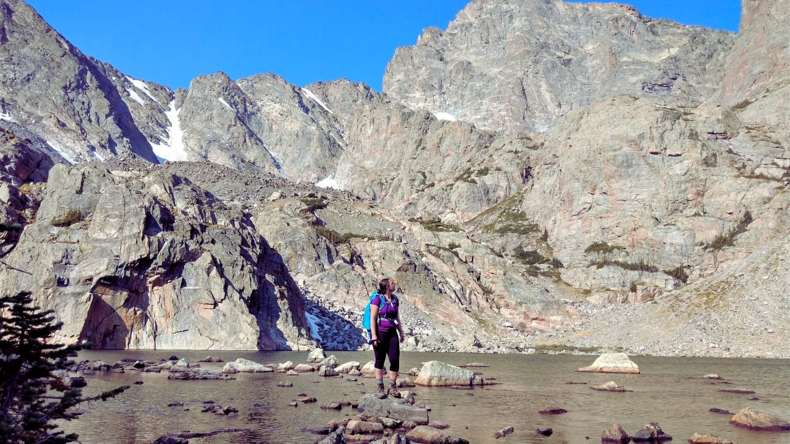 A person stands on a rock, gazing at a majestic mountain in the background under a clear blue sky.