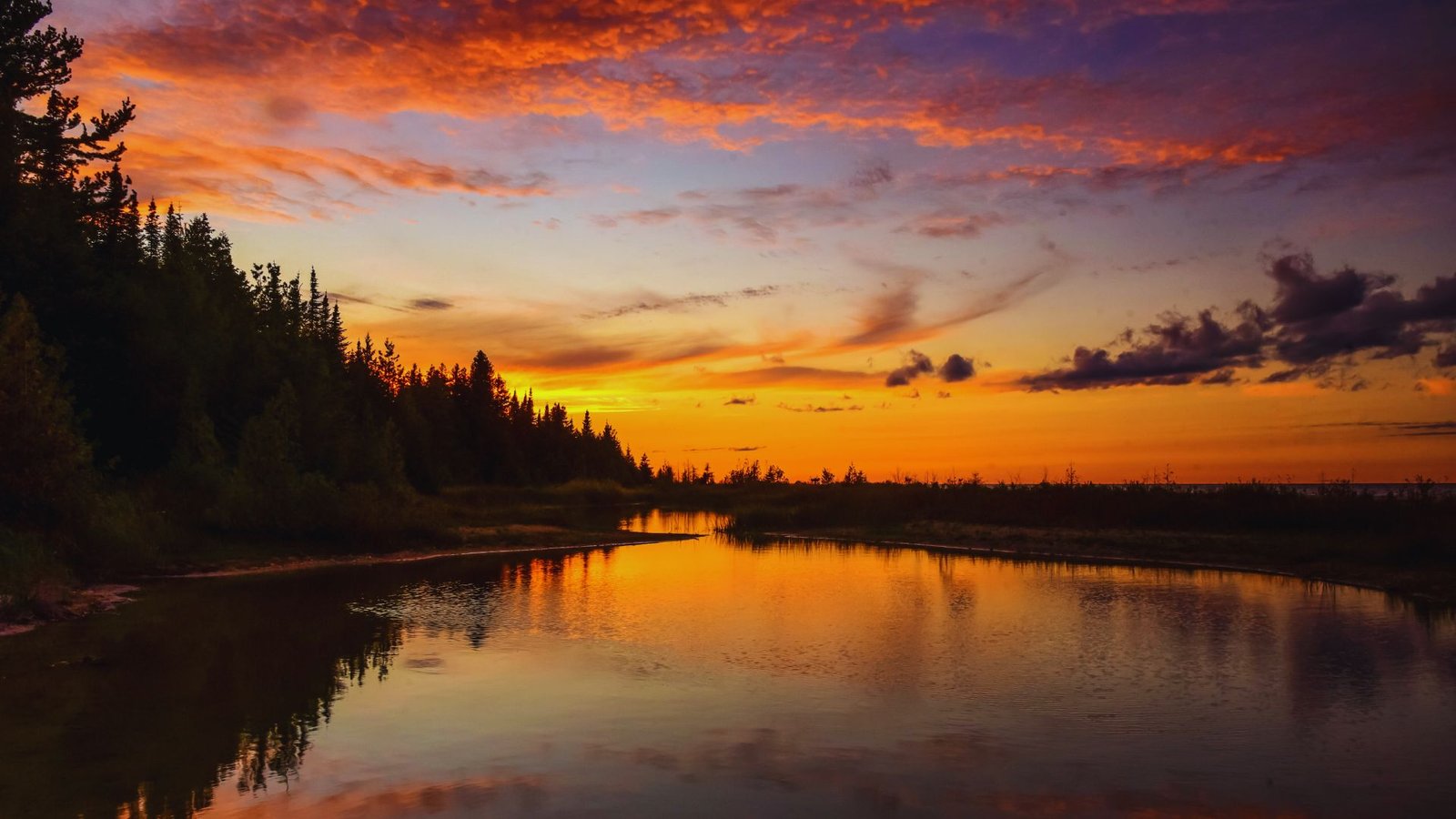 A vibrant sunset casts warm hues over the Yellowstone River, reflecting the colors in the calm water below.