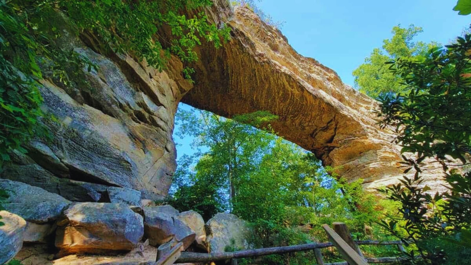 A stone archway with a wooden bridge spans beneath it, surrounded by greenery.