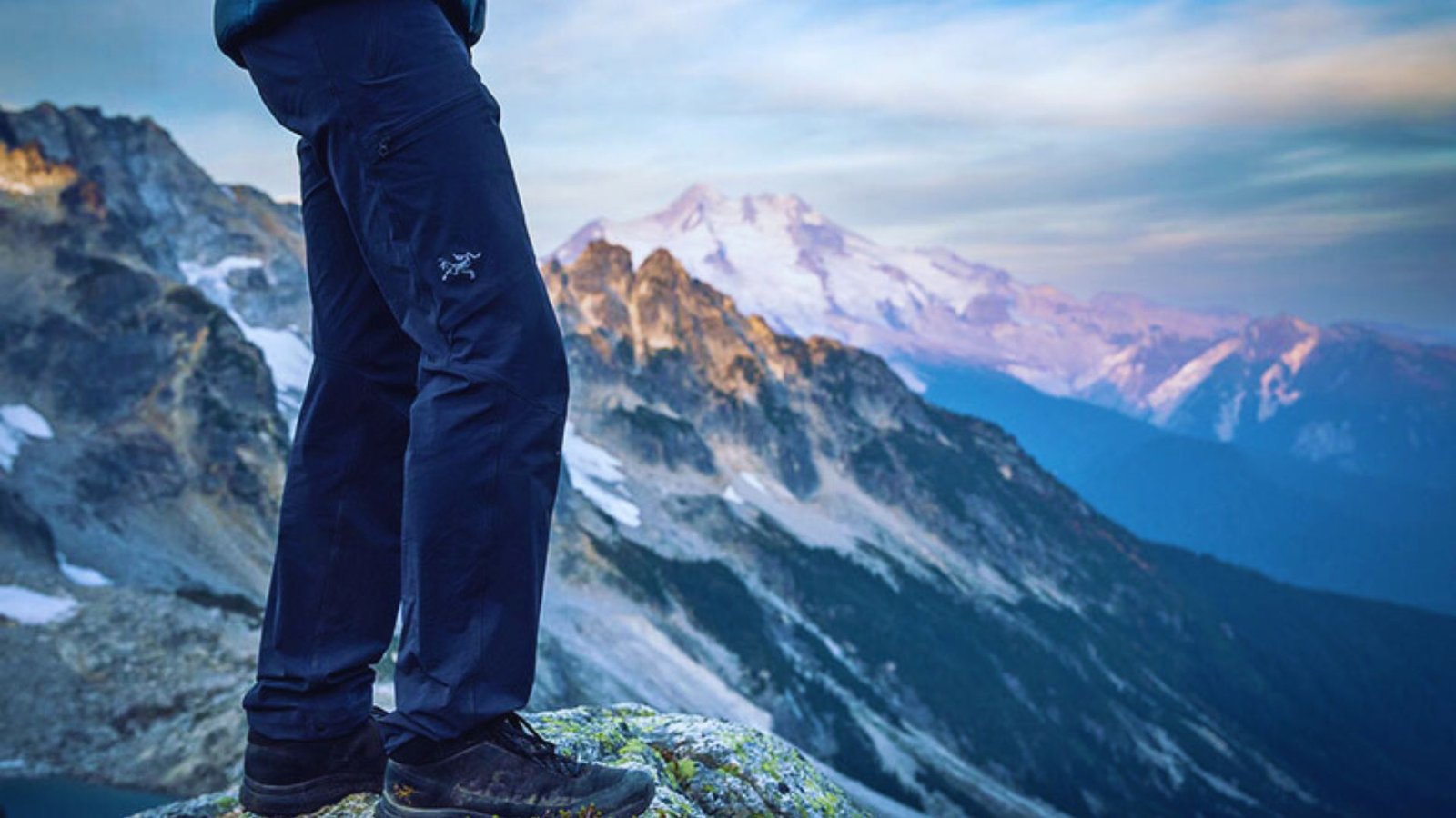 A person stands triumphantly on a mountain peak, overlooking a breathtaking view of distant mountain ranges.