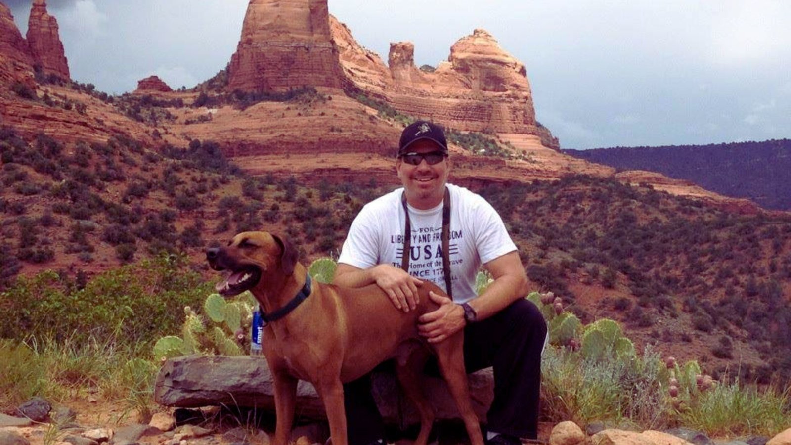 A man and his dog smile for a photo with a majestic mountain backdrop.