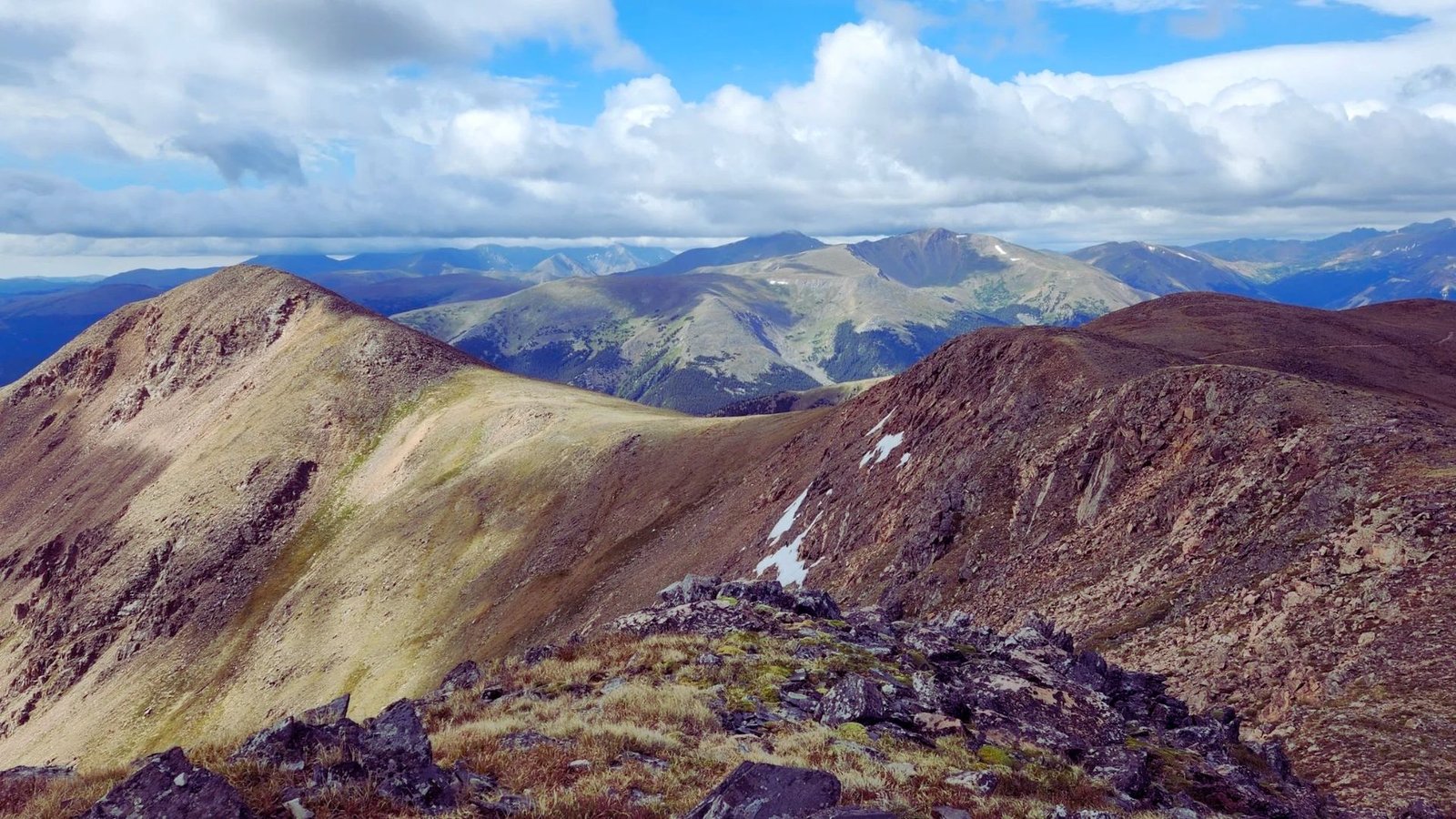 Panoramic view from the mountain summit, showcasing vast landscapes and distant peaks under a clear blue sky.