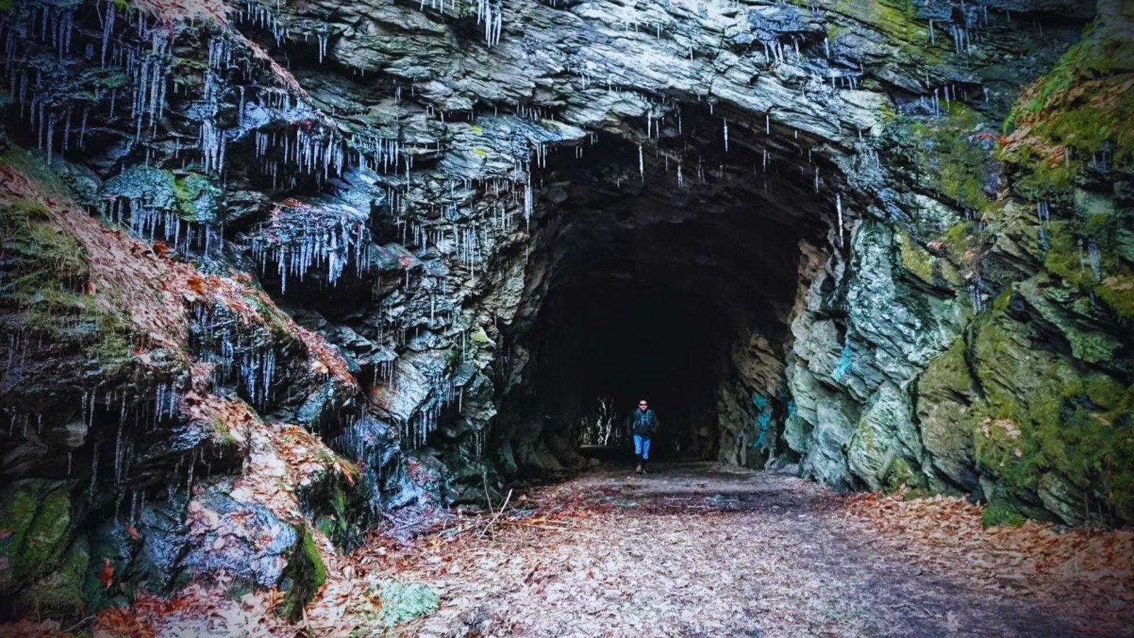 A person walks through a tunnel adorned with icicles hanging from the ceiling, creating a chilly, icy atmosphere