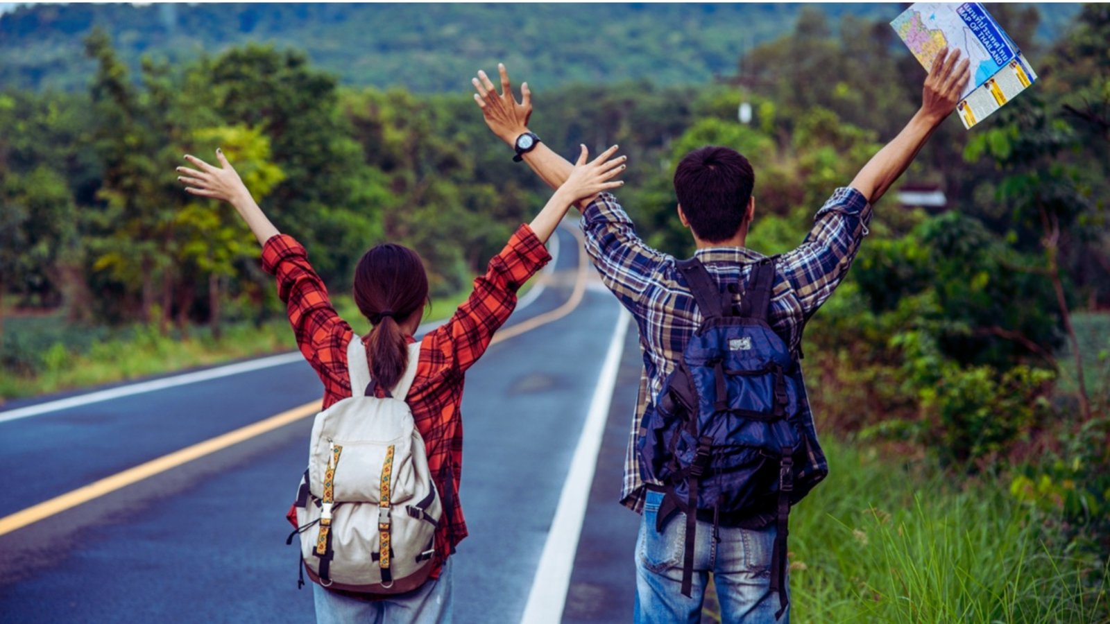  A joyful couple on a road trip, holding a map and raising their hands in excitement while traveling together.