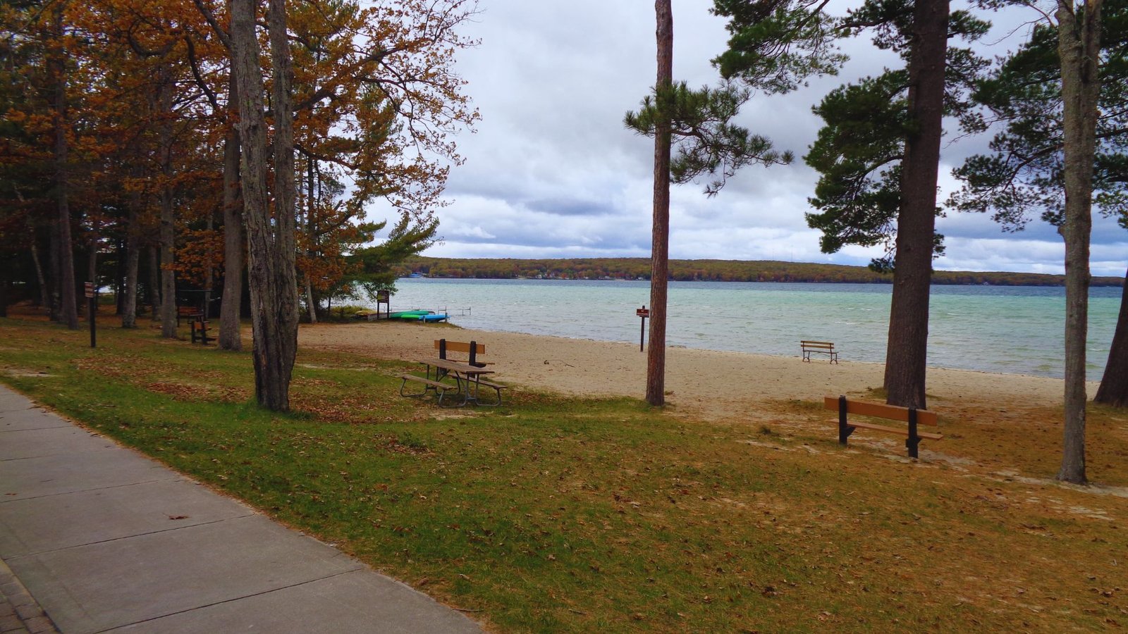  A wooden bench on green grass beside a sandy beach, with gentle waves lapping at the shore in the background.