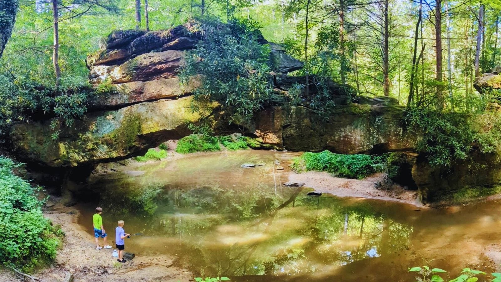 Two individuals stand before a large rock formation, showcasing the natural landscape and their scale against the rocks.