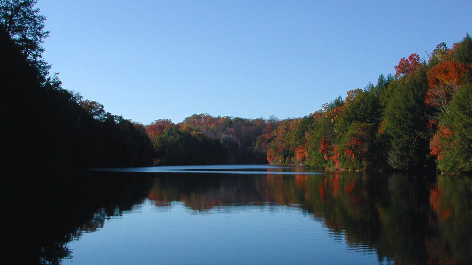 A serene lake framed by colorful autumn trees, reflecting the vibrant fall foliage in the calm water.
