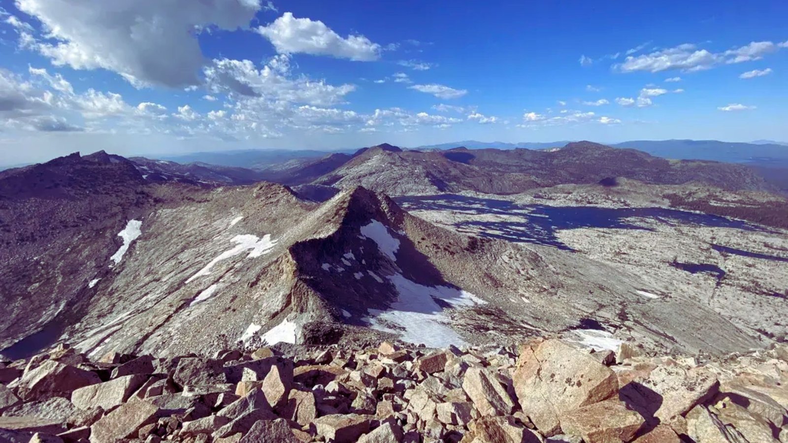  A panoramic view of distant mountains from the summit of a mountain, showcasing rugged peaks under a clear blue sky.