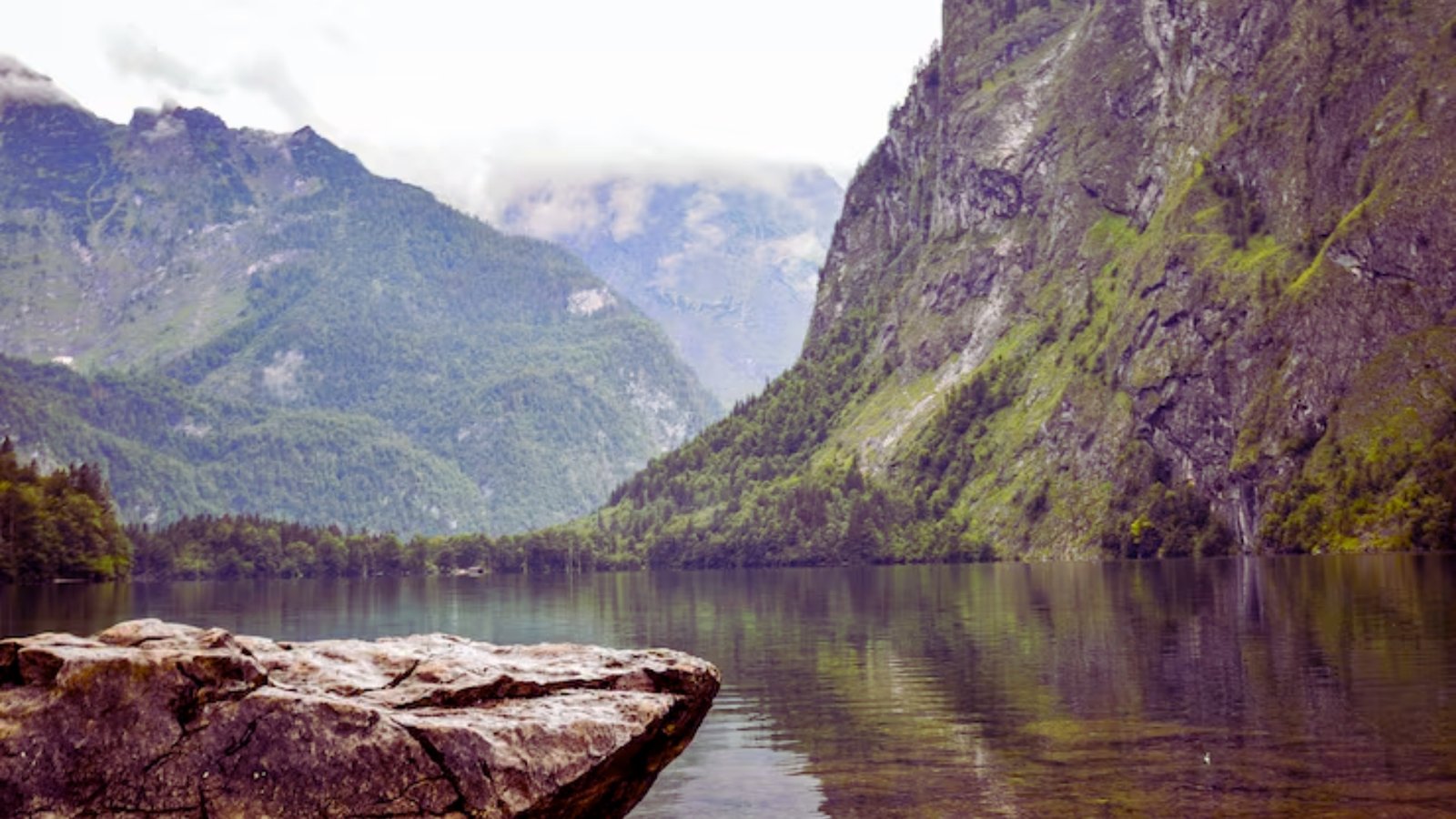 . A serene lake nestled among towering mountains and lush green trees under a clear blue sky.