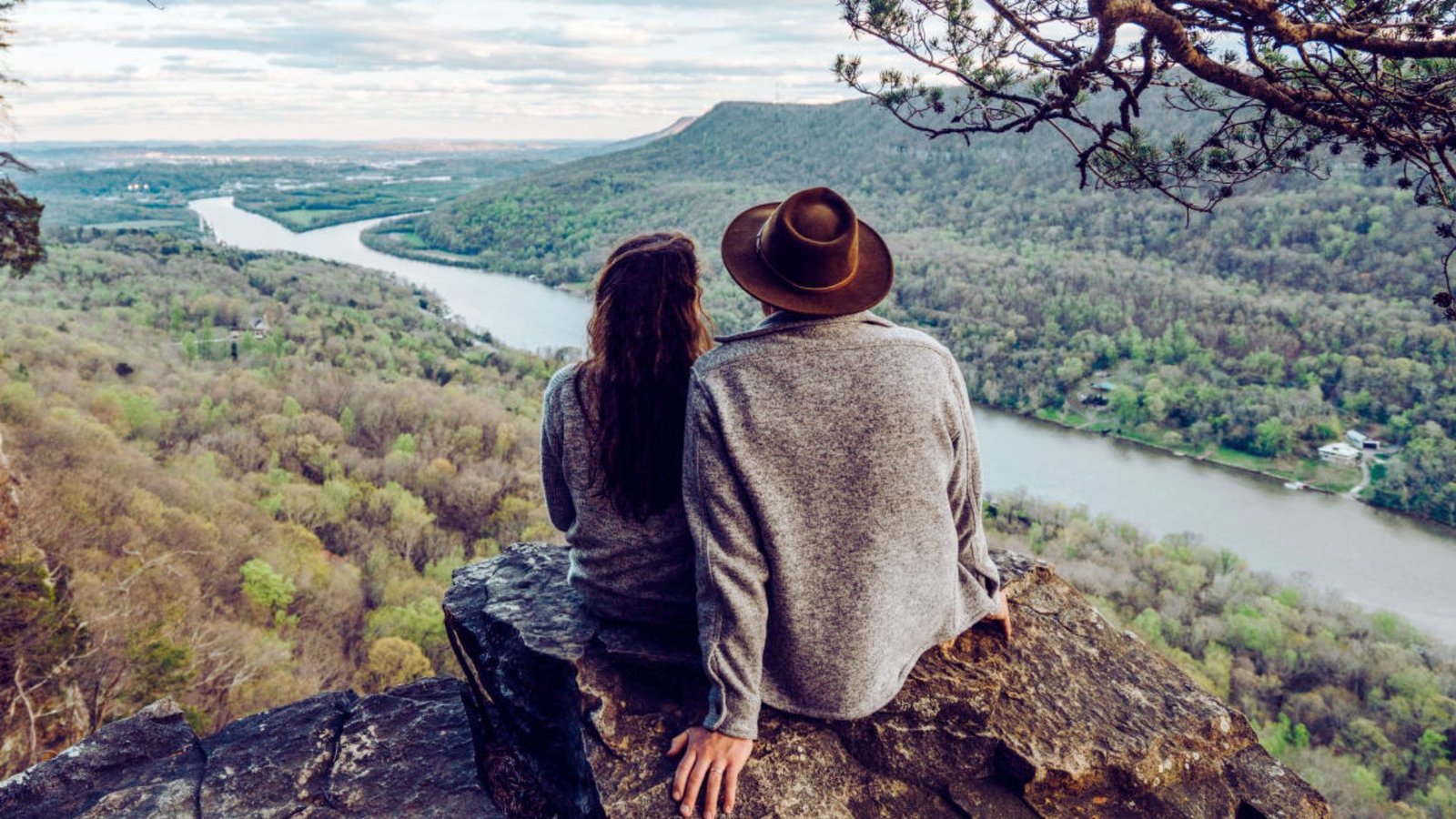 A couple perched on a rock, enjoying a scenic view of a river below them.