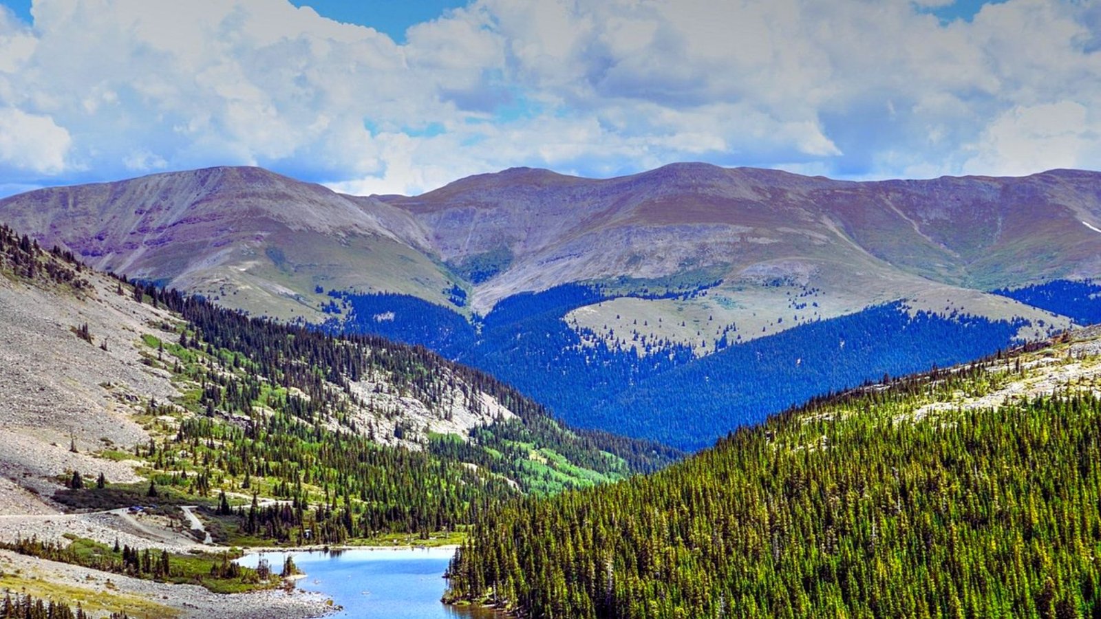 Scenic view of majestic mountains reflecting in a serene body of water, surrounded by lush greenery.