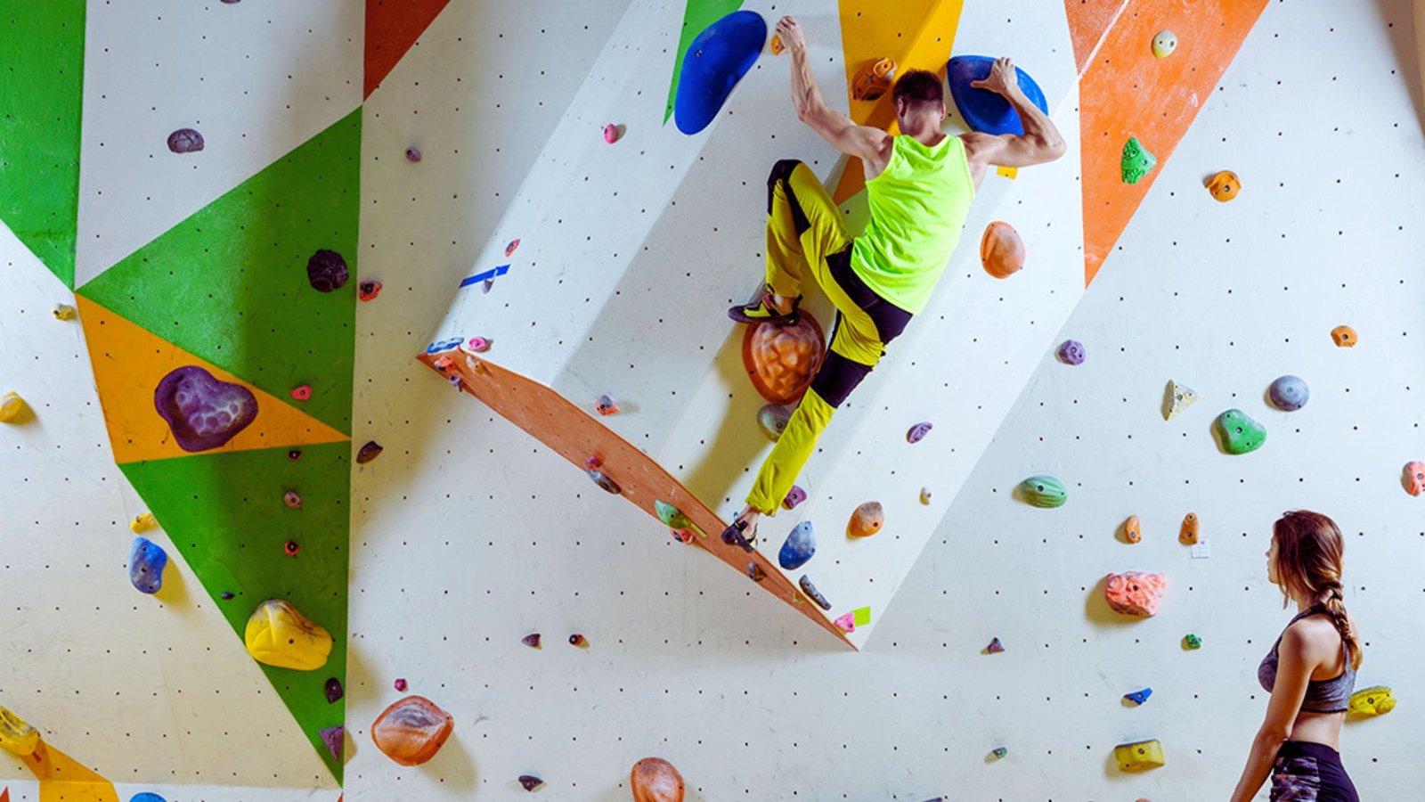 A man and woman engaged in rock climbing, navigating a vertical wall with climbing holds and harnesses.