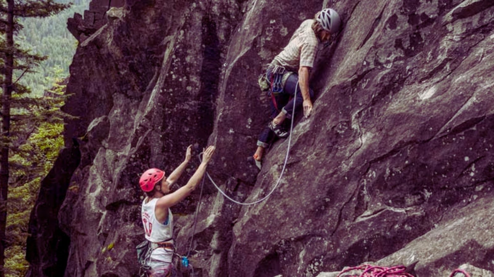 Two climbers ascend a rocky cliff, secured by a rope, showcasing teamwork and determination in a challenging environment.