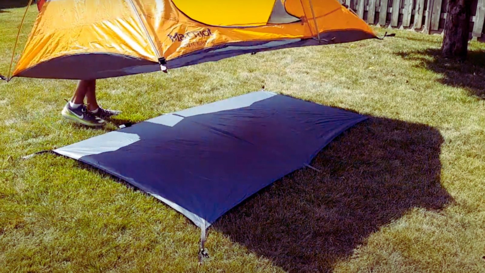 A person stands beside a tent on green grass, enjoying the outdoor setting