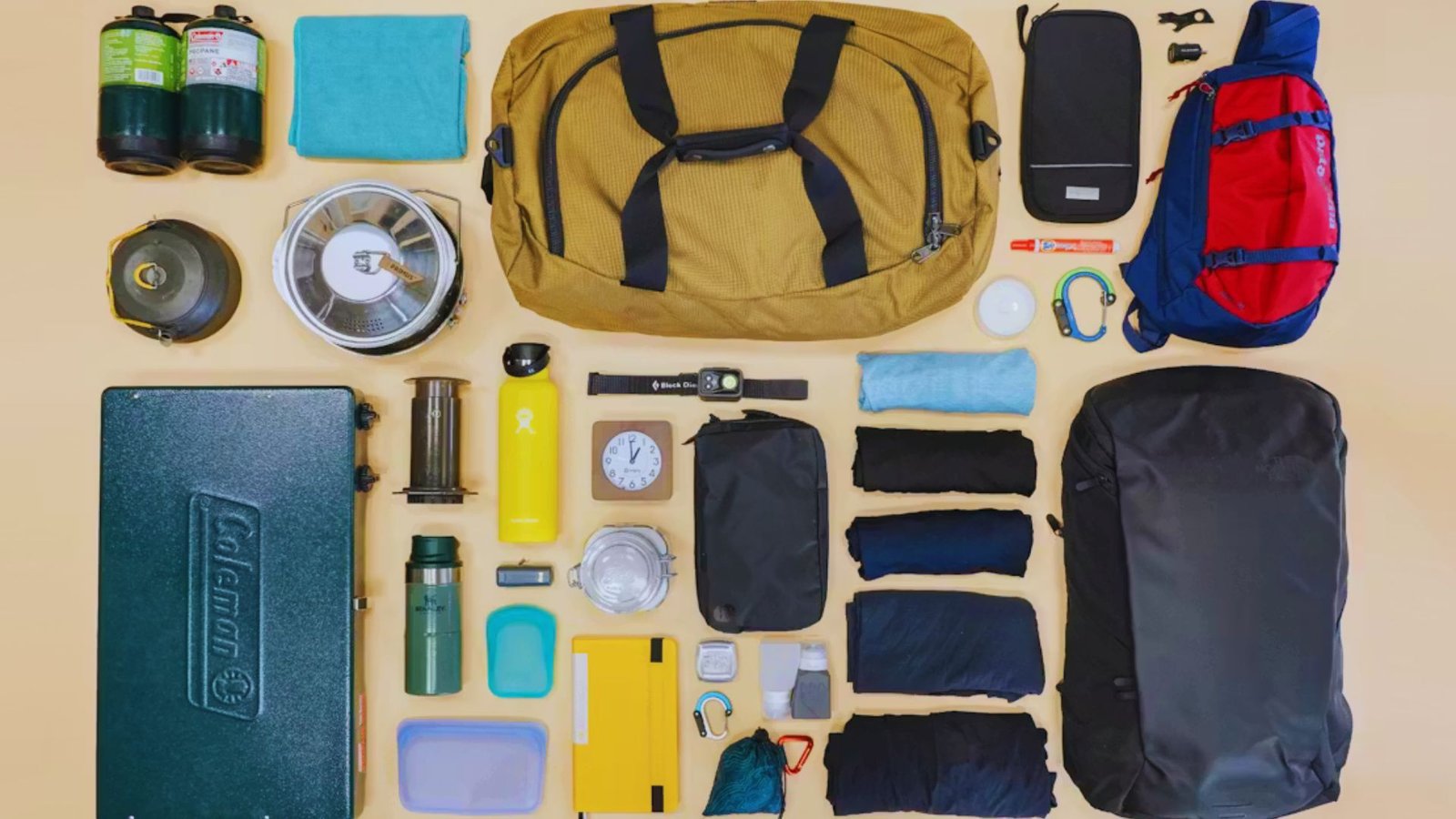 A table displaying essential camping gear from a backpack, including a tent, sleeping bag, and cooking supplies.
