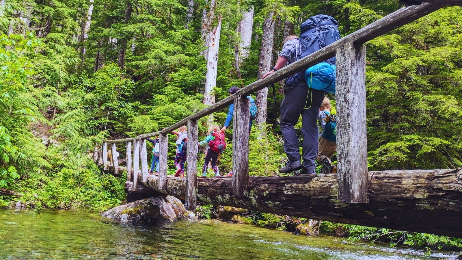 People walking across a wooden bridge on the Barclay Lake Trail in a lush forest setting in Washington.
