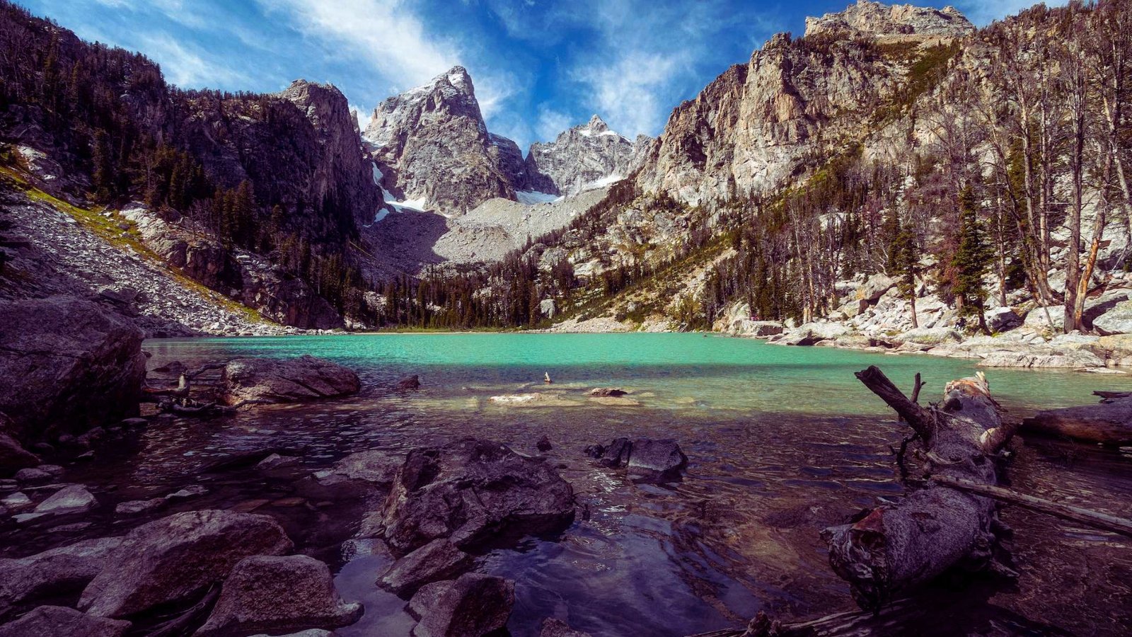 A serene lake nestled among towering mountains and rugged rocks under a clear blue sky.