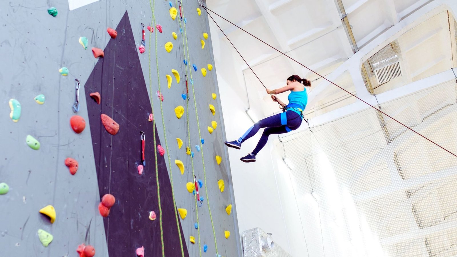 A woman is climbing a rock wall, showcasing her strength and determination in an outdoor climbing environment.