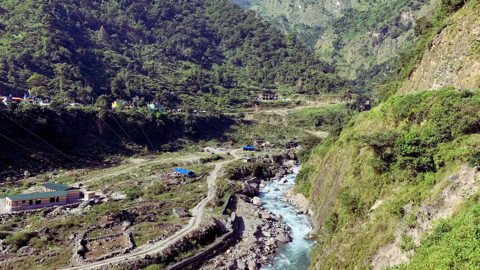 A serene river flows through a lush valley surrounded by majestic mountains under a clear blue sky.
