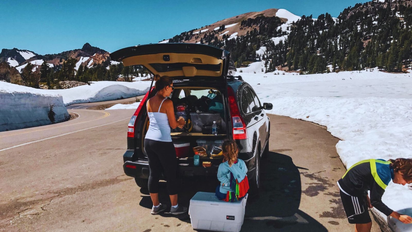 A woman and a child are packing a car with luggage, preparing for a road trip camping adventure.
