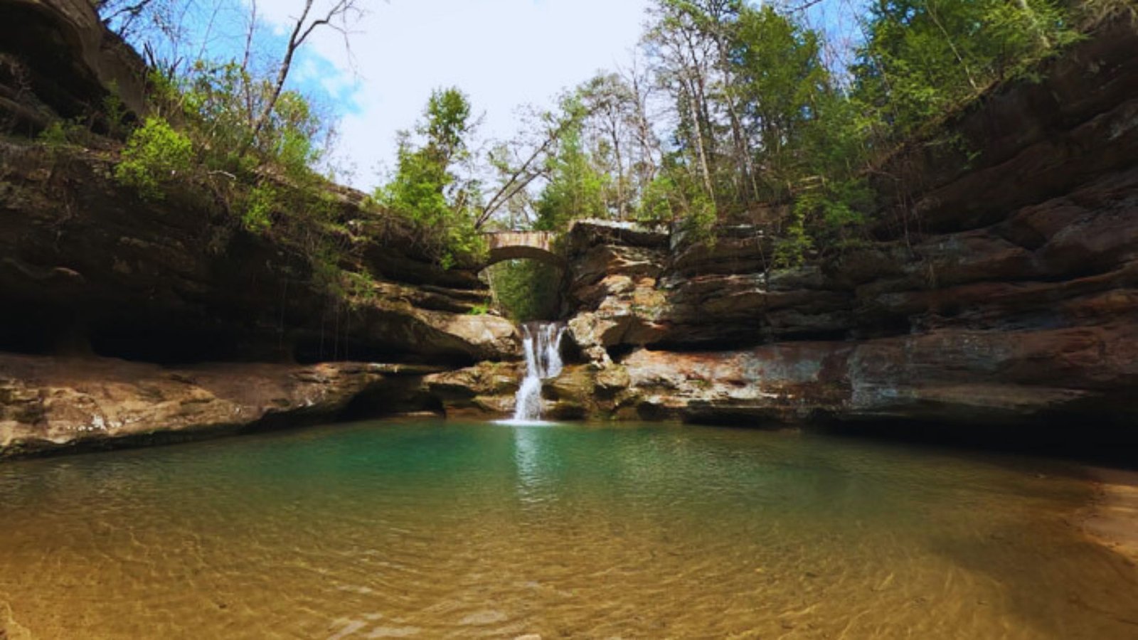 A group of people stands on a cliff, gazing at a majestic waterfall cascading into a lush valley below.