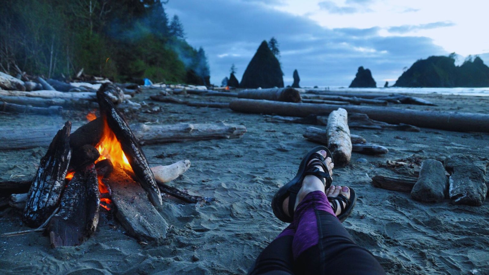 A person sitting on Shi Shi Beach with their feet resting in the warm sand, enjoying the coastal scenery.
