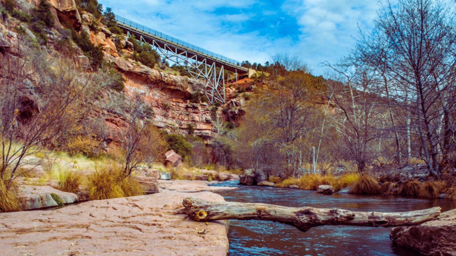 . A man strolls beside a river flowing through a canyon, with towering cliffs rising on either side.