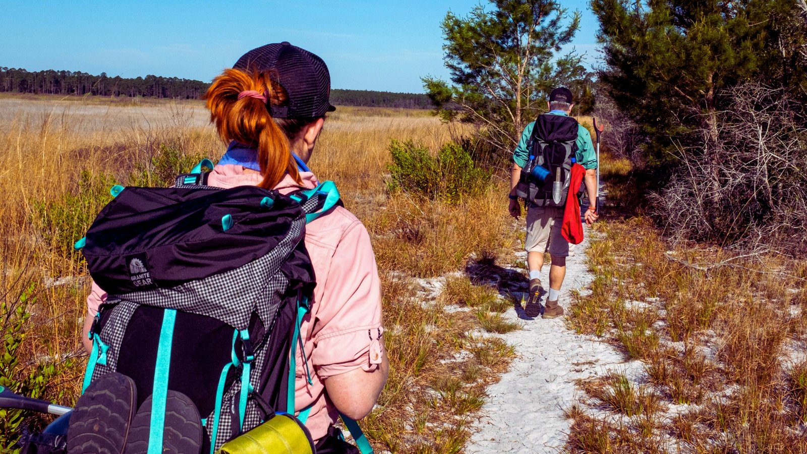 Two hikers with backpacks trekking on a wooded trail, enjoying the outdoors.