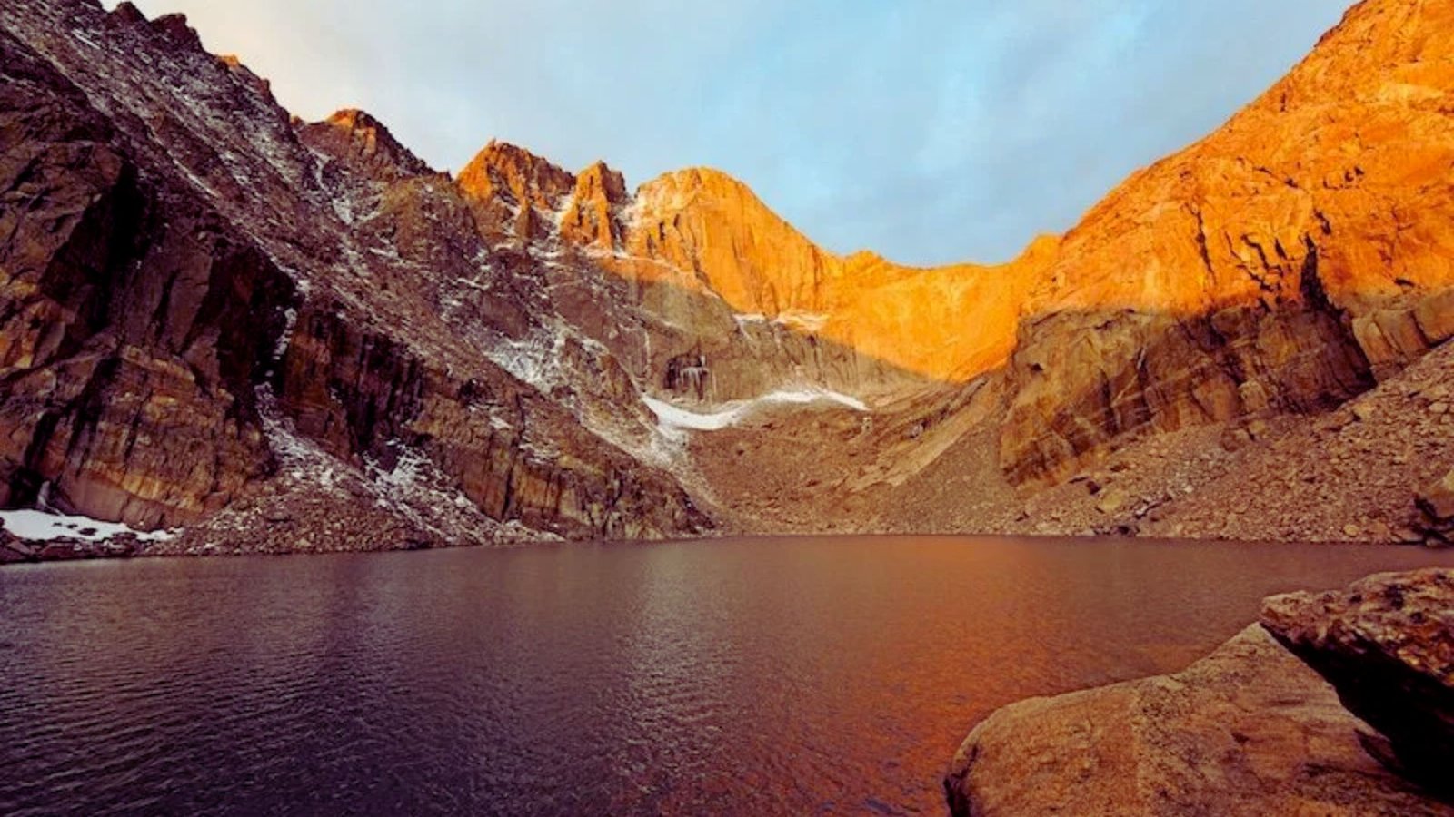 A serene mountain lake nestled among snow-covered rocks and peaks, reflecting the clear blue sky above.