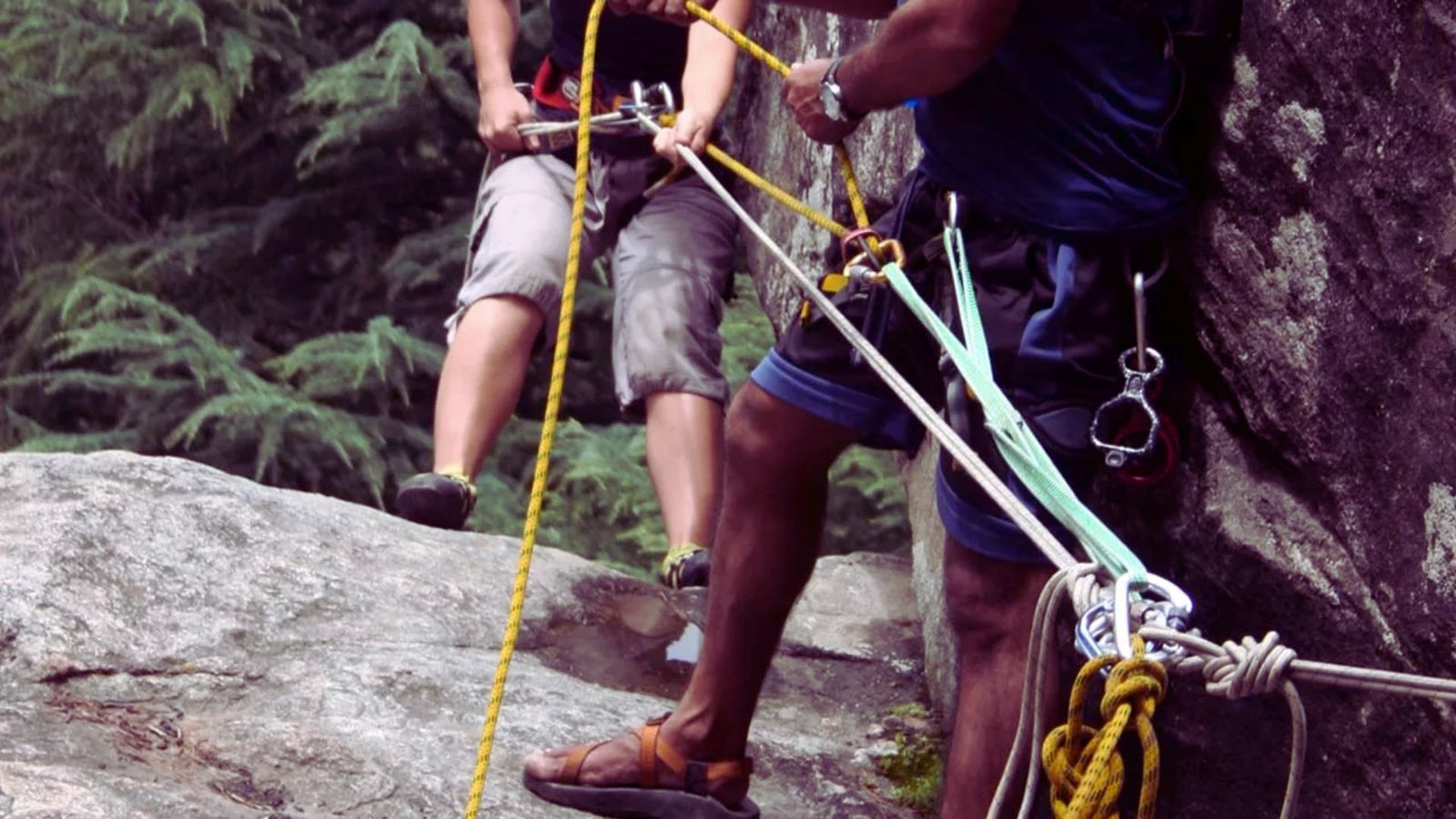 Two climbers ascend a steep mountain using ropes, showcasing teamwork and determination against a rugged landscape.
