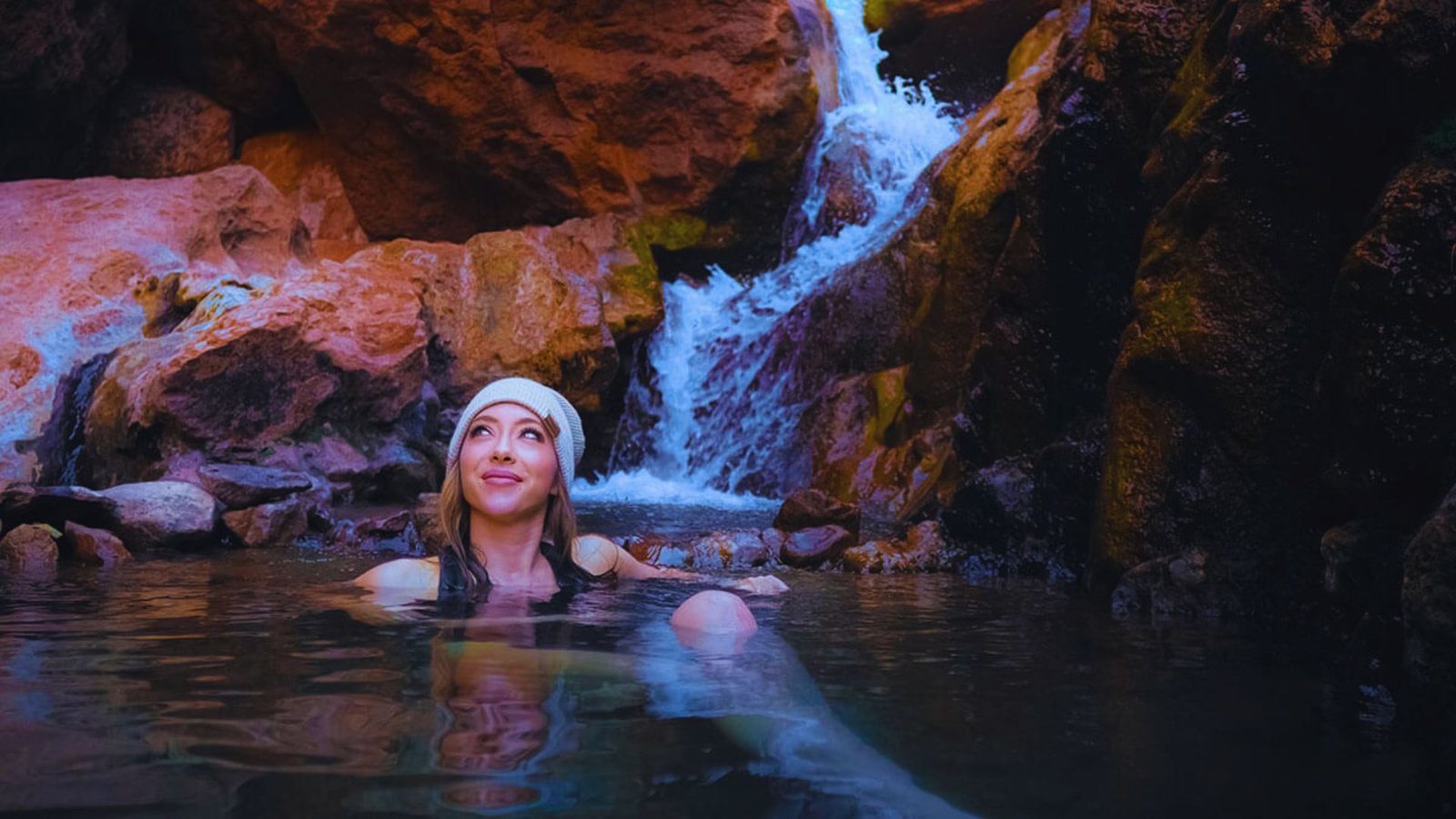 A woman relaxes in a bathtub with a serene waterfall cascading in the background.