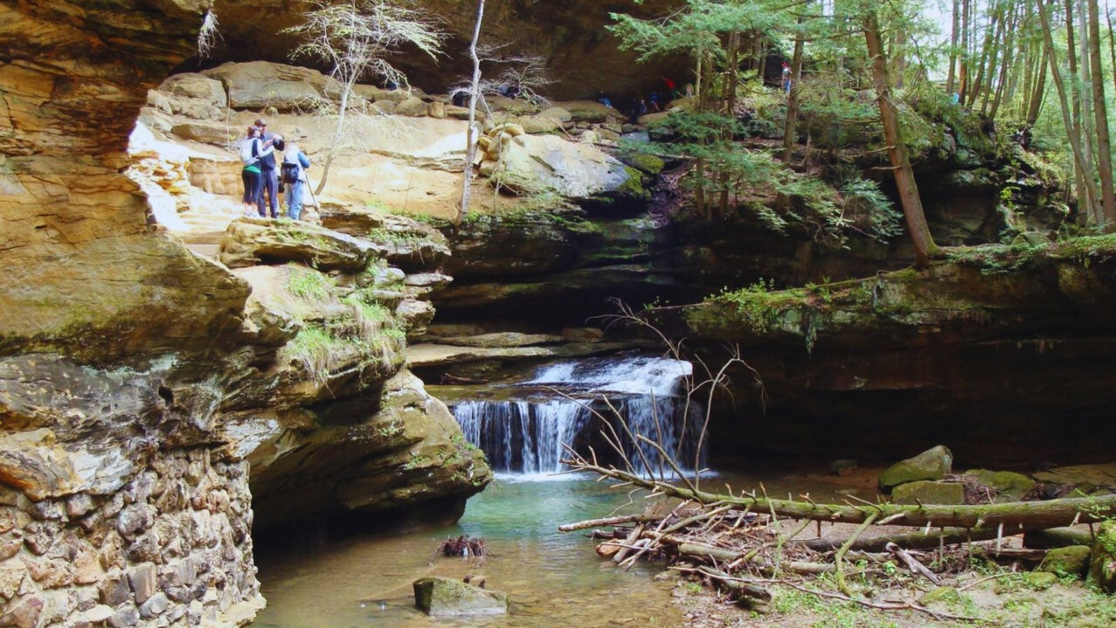 A group of people stands on a cliff, gazing at a majestic waterfall cascading into a lush valley below.