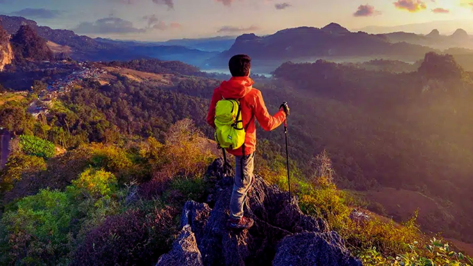 Man on a mountain summit, surveying a beautiful valley landscape, with lush greenery and a clear horizon.