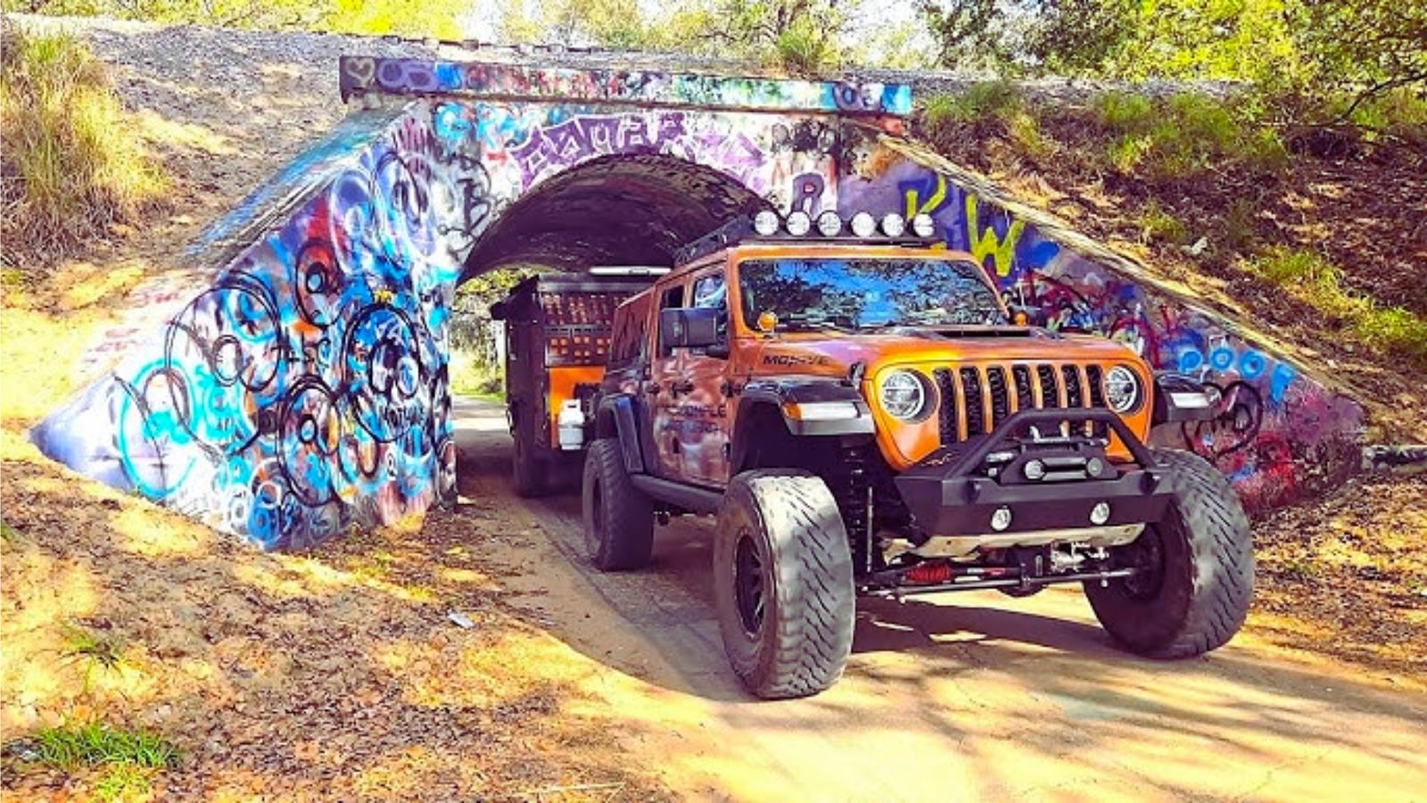 A jeep sits under a tunnel adorned with vibrant graffiti, highlighting urban culture and exploration.