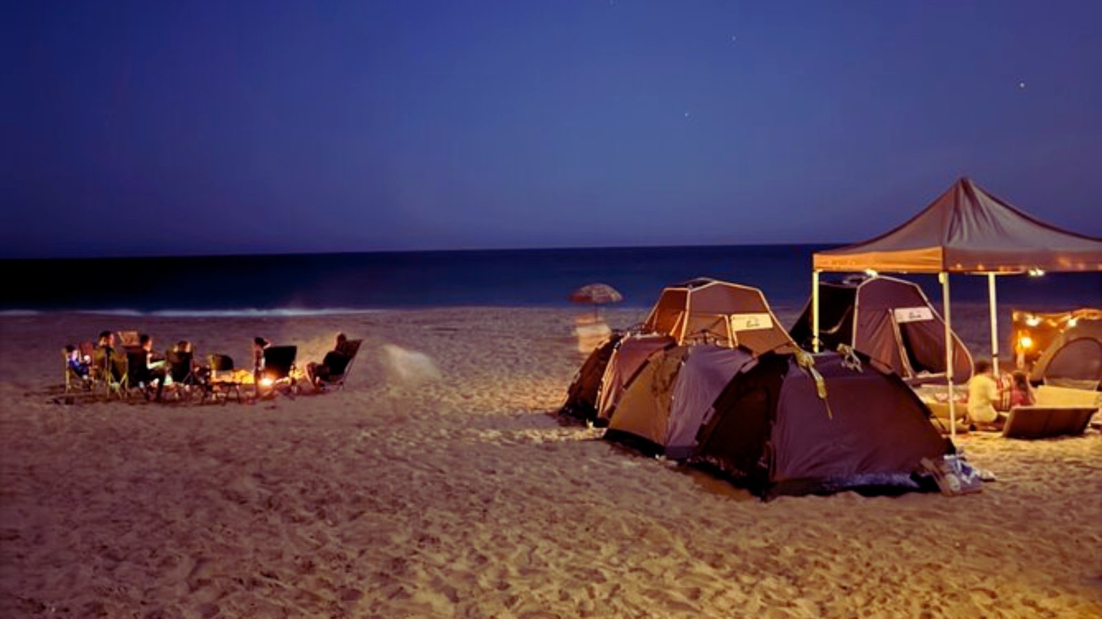 A group of tents set up on the beach, illuminated by moonlight, creating a serene nighttime atmosphere.